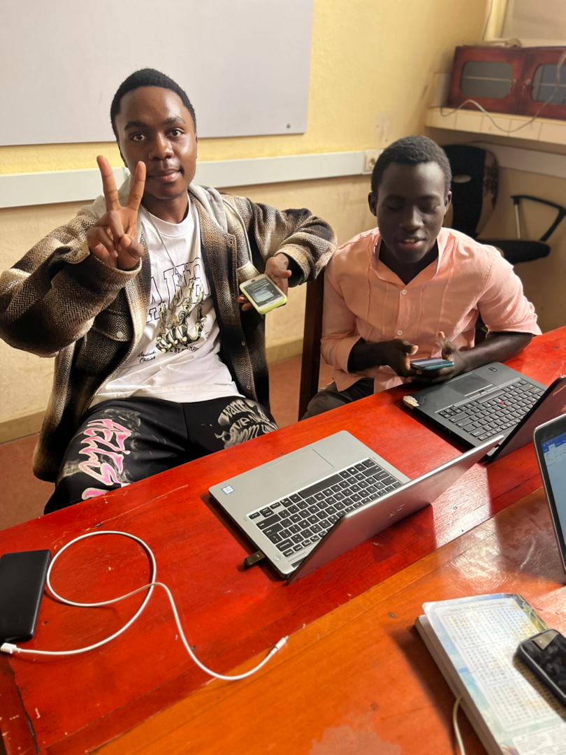 Two hackathon participants at a desk with laptops and phones
